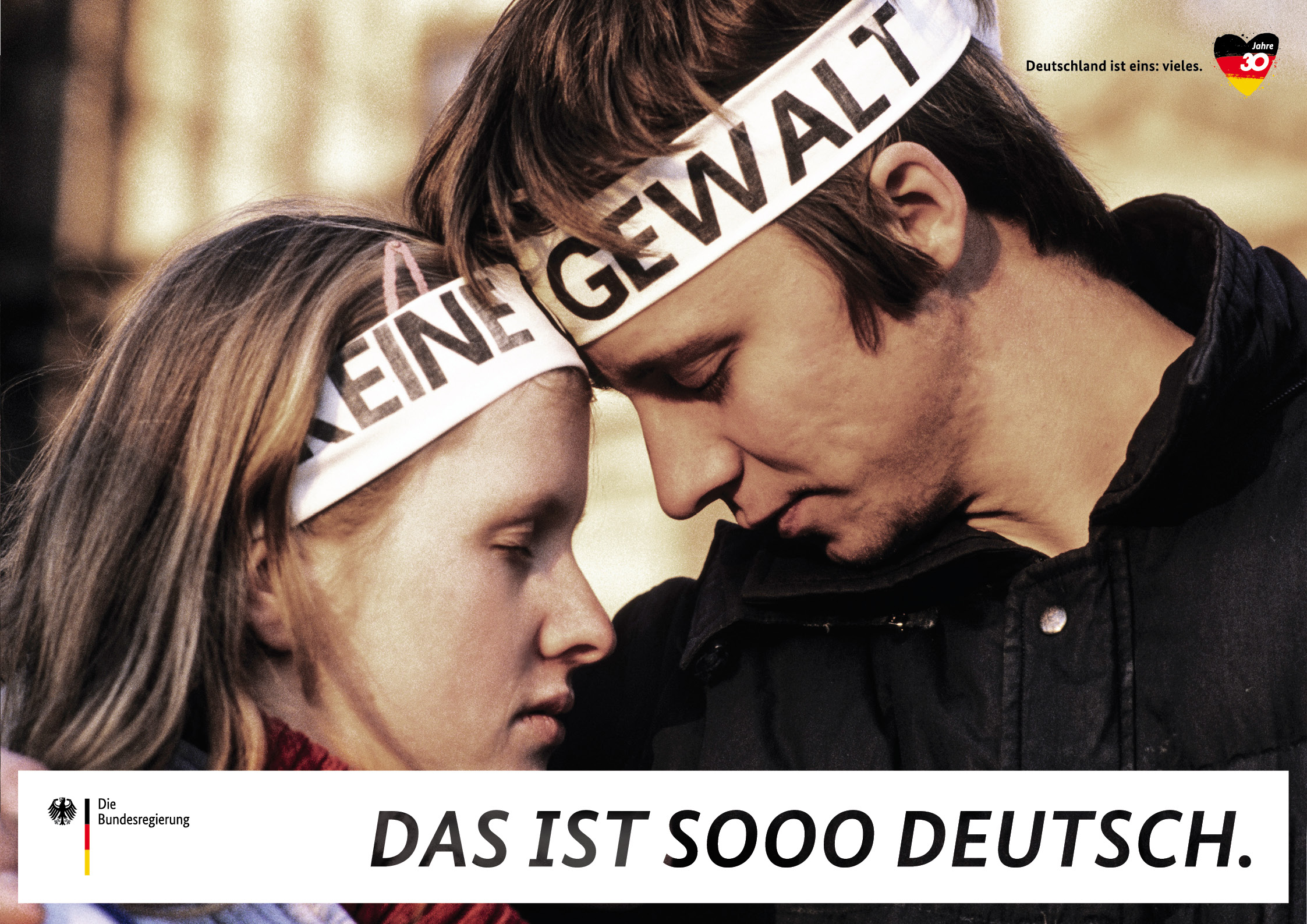 Ein historisches Foto von einem Paar, das mit Stirnbändern mit der Aufschrift "Keine Gewalt" demonstriert, auf einem Plakat der Kampagne "Deutschland ist eins: vieles".