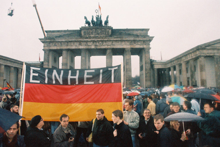 Menschen mit einem Transparent „Einheit“ (im Regen)vor dem Brandenburger Tor.