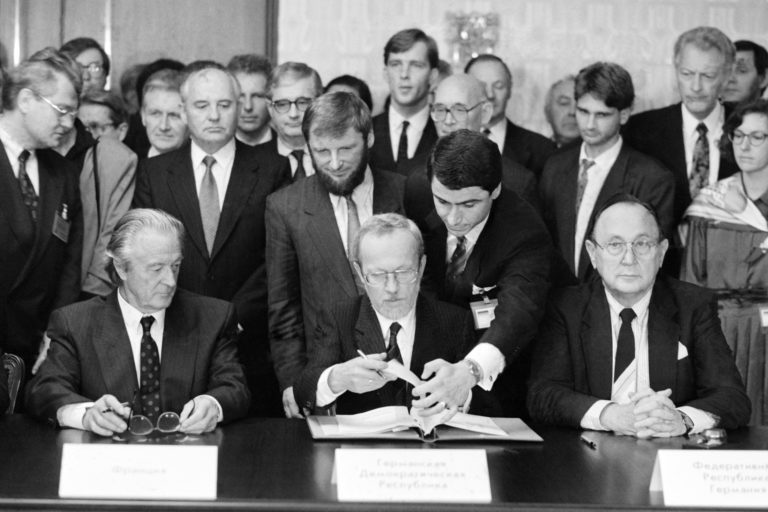 Lothar de Maizière, Ministerpräsident der DDR, unterzeichnet den „Vertrag über die abschließende Regelung in Bezug auf Deutschland“ im Hotel Oktjabrskaja (r.: Hans-Dietrich Genscher, Bundesminister des Auswärtigen der BRD; l.: Roland Dumas, Außenminister Frankreich; dahinter 2.v.l.: Michail Gorbatschow,  Staatspräsident der Sowjetunion).